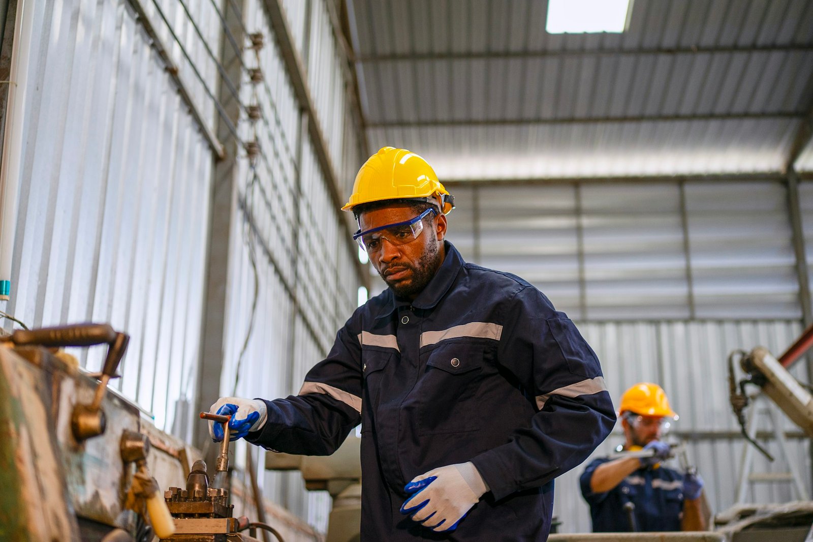 Blue collar workers at machine shop with welding robot arm.